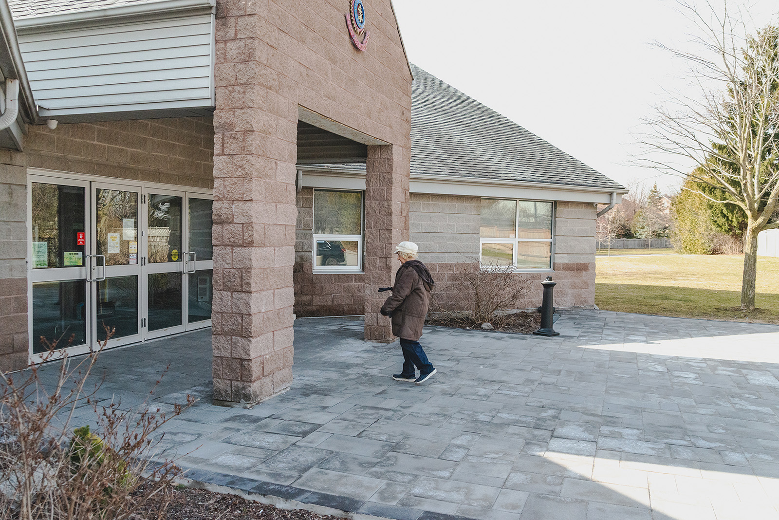 Exterior entrance of The Salvation Army Whitby Community Church building with glass doors and stone pillars, as a person walks along a paved walkway toward the entrance, with open green space and trees visible in the background.