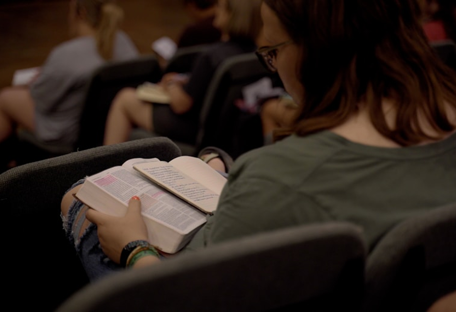 Close-up of a person seated in a church holding and reading an open Bible.